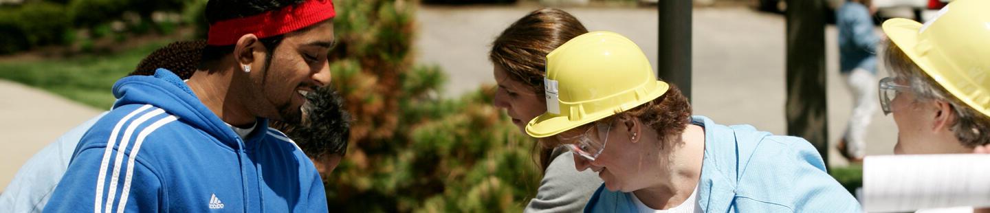 male in blue addidas sweatshirt and red headband with women in yellow hard hats